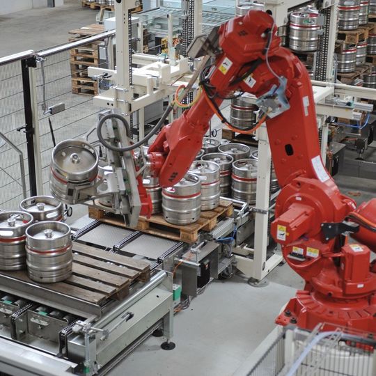 Bild 1: Statt der auf DIN-Kegs begrenzten Palettenanlagen übernehmen jetzt zwei Roboter das Ent- und Beladen inklusive Palettenhandling. Bild 1: Statt der auf DIN-Kegs begrenzten Palettenanlagen übernehmen jetzt zwei Roboter das Ent- und Beladen inklusive Palettenhandling.