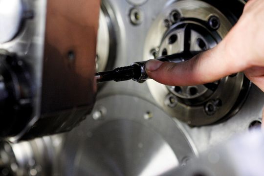 Blick auf den Fertigungsprozess ab Stange und auf die aufgeschnittene Gewindebuchse. Der Gewindeschneider muss zirka 20 mm in das Werkstück eintauchen, bevor es ans Zerspanen geht. Dank Sackloch (ab Stange) und 20-bar-Hochdruckkühlung werden die Späne sicher aus der Prozesszone nach hinten abgeführt. Blick auf den Fertigungsprozess ab Stange und auf die aufgeschnittene Gewindebuchse. Der Gewindeschneider muss zirka 20 mm in das Werkstück eintauchen, bevor es ans Zerspanen geht. Dank Sackloch (ab Stange) und 20-bar-Hochdruckkühlung werden die Späne sicher aus der Prozesszone nach hinten abgeführt.