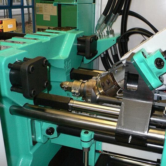 Das Bild zeigt die beiden im Winkel angeordneten Spritzzylinder für die zu verarbeitenden Materialien. Das Bild zeigt die beiden im Winkel angeordneten Spritzzylinder für die zu verarbeitenden Materialien.