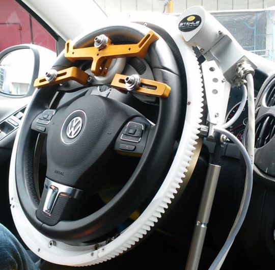 Der Lenkroboter der Firma Stähle kann nachträglich in Autos verbaut werden. Er klemmt sich um das Lenkrad sowie in den Fußraum zu Brems- und Gaspedal. Der Lenkroboter der Firma Stähle kann nachträglich in Autos verbaut werden. Er klemmt sich um das Lenkrad sowie in den Fußraum zu Brems- und Gaspedal.