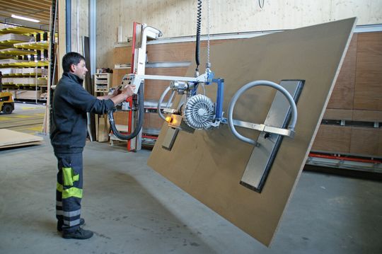 Eine grosse Holzplatte wird vom Stapler angehoben, um 90° gekippt und für den Zuschnitt zur Vertikalsäge gefahren. Gut sichtbar sind die in Längsrichtung verstellbaren um 90° drehbaren Saugflächen. Eine grosse Holzplatte wird vom Stapler angehoben, um 90° gekippt und für den Zuschnitt zur Vertikalsäge gefahren. Gut sichtbar sind die in Längsrichtung verstellbaren um 90° drehbaren Saugflächen.