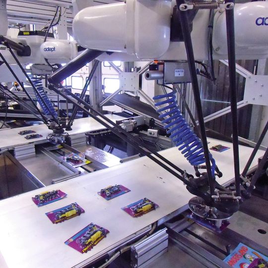 Bild 1: Aufkleben im Vorbeiflug: Zwei Deltaroboter greifen die Gimmicks vom Zuführband und kleben sie mit einem Druckluftimpuls auf die vorbeilaufenden Zeitschriften. Bild 1: Aufkleben im Vorbeiflug: Zwei Deltaroboter greifen die Gimmicks vom Zuführband und kleben sie mit einem Druckluftimpuls auf die vorbeilaufenden Zeitschriften.