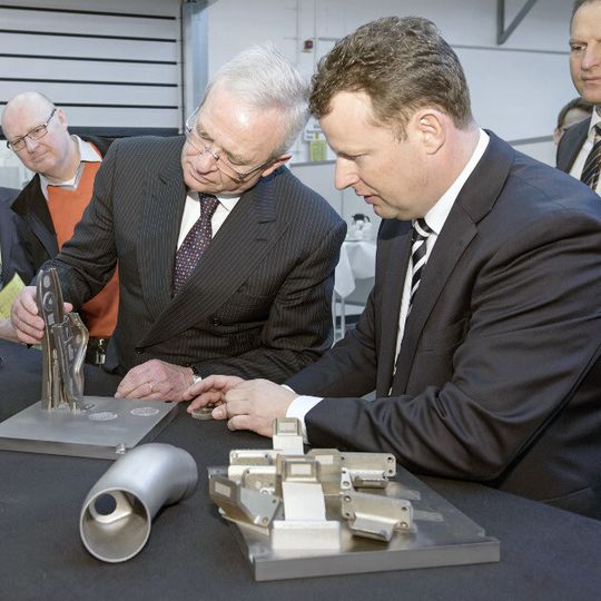 Prof. Dr. Winterkorn prüft in Wolfsburg ein mit dem metallischen 3-D-Drucker hergestelltes Bauteil.