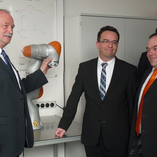 Nördlingens Oberbürgermeister Hermann Faul (links im Bild) probt den Handschlag mit dem innovativen Leichtbauroboter LBR iiwa von KUKA. Die sichere Mensch-Roboter-Kollaboration (MRK) soll am MRK TecCamp in Anwenderszenarien anschaulich demonstriert, für Studierende aufbereitet und für künftige Anwendungen im Mittelstand bedarfsgerecht optimiert werden.