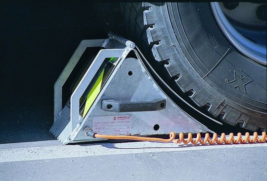 Bild 1: Elektrokeile sind über ein Spiralkabel mit der Rampensteuerung verbunden. Erst wenn sie fachgerecht unter das Rad gelegt worden sind, wird der Verladevorgang freigegeben. Bild 1: Elektrokeile sind über ein Spiralkabel mit der Rampensteuerung verbunden. Erst wenn sie fachgerecht unter das Rad gelegt worden sind, wird der Verladevorgang freigegeben.