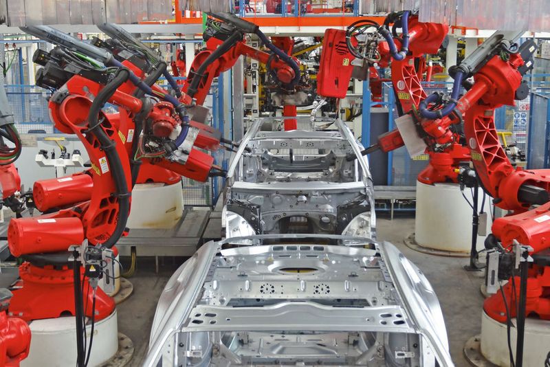 Beim Anbringen und Befestigen von Karosserieteilen bilden Roboter ein Spalier. Sie stehen in dichten Reihen nebeneinander und schweißen, nieten, falzen, bringen Bolzen und manches mehr – teilweise in parallel laufenden Prozessen.
