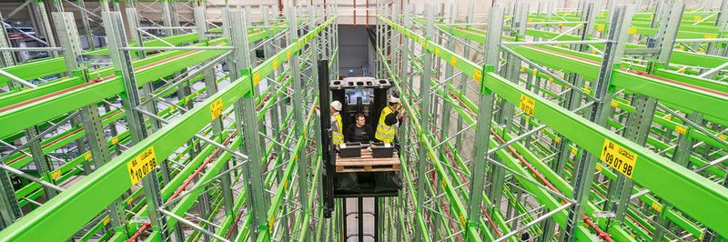 Im Schmalgang-Palettenregal bekleben zwei Monteure die Regalreihen parallel mit den Etiketten.