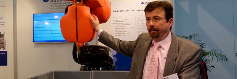 Christoph Meyer von der BGHM erklärt, dass kapazitive Sensoren durch eine Veränderung des elektrischen Feldes erkennen, wenn sich eine Hand nähert – und den Roboterarm stoppen.