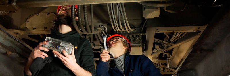 Projektmitarbeiter Silvio Hund (l.) und Maik Wolf (r.) bringen einen energieautarken Sensor am Triebdrehgestell einer Straßenbahn der Leipziger Verkehrsbetriebe an.