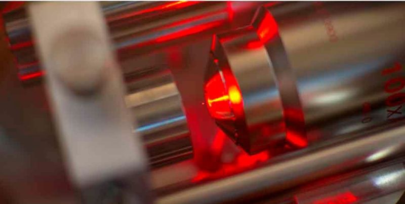 Ein Mikroskop-Objektiv (rechts) bündelt Laserlicht zu einer optischen Pinzette, von der ein Nanokügelchen (winziger roter Punkt in der Bildmitte) in der Schwebe gehalten wird. (Bild: ETH Zürich / Erik Hebestreit und Vijay Jain)