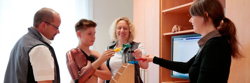 Nick übt den Dreipunkt-Griff. V.l.n.r.: Stefan Reinelt, Spezialist für Armprothetik, zusammen mit Nick Deike, der Ergotherapeutin Daniela Wüstefeld und der Orthopädiemechaniker-Meisterin Julia Bötticher.