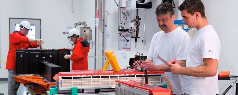 Im Vordergrund prüfen Mitarbeiter Spannungsabgriffe von Batteriezellen, im Hintergrund findet die elektrische Endmontage einer Batterie für den R8 E-Tron statt.