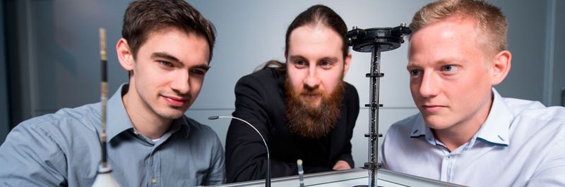 Die Doktoranden Dominik Scholtes (l.), Rouven Britz und Yannik Goergen (r.) aus Prof. Stefan Seeleckes Team mit Prototypen der biegsamen Roboterarme, die auf der Hannover Messe zu sehen sein werden.
