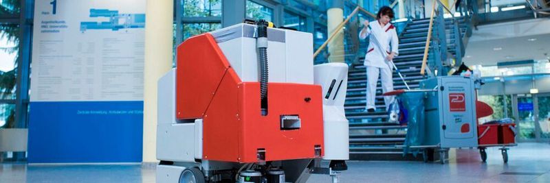 Im Vordergrund sieht man den Reinigungsroboter, wie er eigenständig den Boden in einem Krankenhaus nass wischt.