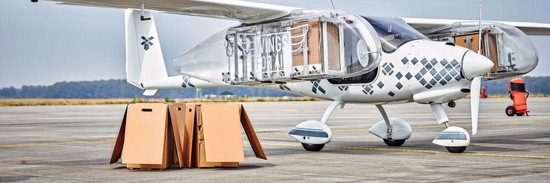 Flugzeug mit biologisch abbaubaren Kartons, die bei ihrem Abwurf automatisch Flügelklappen für ihren sanften Sinkflug öffnen können.