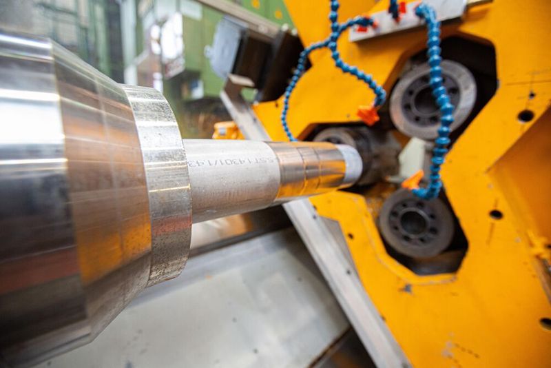 Drückwalzen: Die Spindel (vorne links) dreht das Stahlbauteil, das von den drei Walzen im Hintergrund umgeformt wird. Die blauen Leitungen sorgen für ausreichend Kühlschmierstoff.