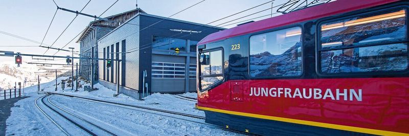 Blick auf die Tore der Werkstatt, während ein Niederflurtriebzug der Jungfraubahn an der Station Eigergletscher durchfährt. Die bisherige Taktzeit wurde von
2 auf 1,5 Stunden reduziert.