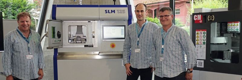 Michel Godel, Frank Gersbach et Frédéric Freiburghaus devant la machine SLM 125 de fabrication additive métallique exposée dans le showroom d'Urma.