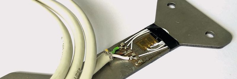 Bild 1:
Konventionell aufgeklebter DMS mit Anschlussleitungen auf Edelstahlbauteil