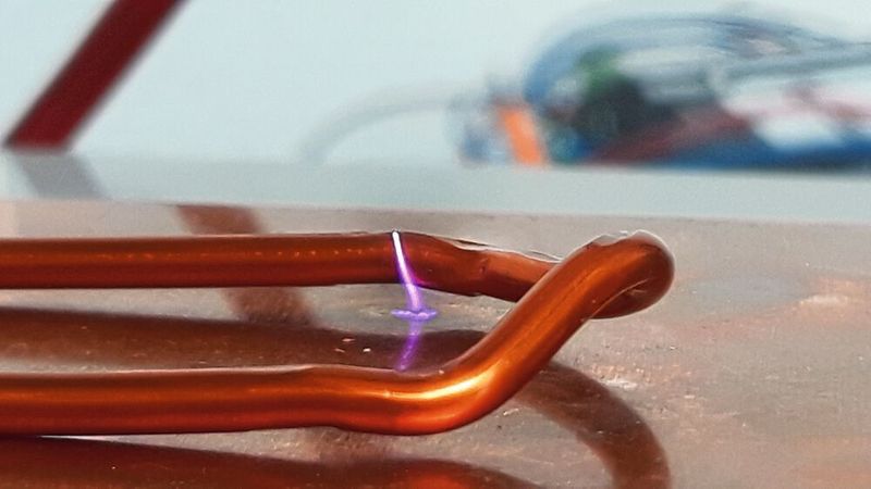 Ein Haarriss in der Isolation eines sogenannten Hairpins wird durch eine violette Glimmentladung sichtbar. Der fließende Strom macht die Beschädigung messbar