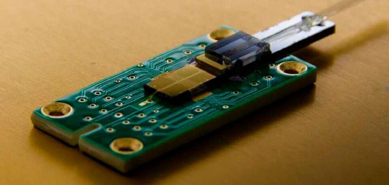 Der Ionenfallen-Chip mit integrierten Wellenleitern. Das Laserlicht wird von den Glasfasern (rechts im Bild) in den Chip eingespeist.