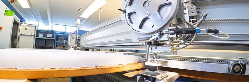 Oberer Nähkopf und Unterfadenstation bilden einen synchronen Verbund in der CNC-gesteuerten Anlage.
