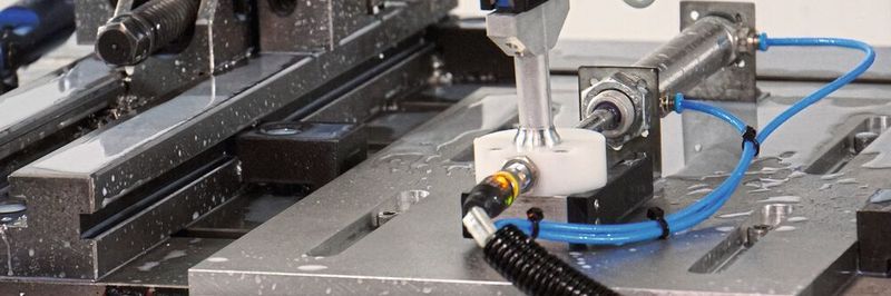 Der Roboter nimmt das Endstück einer Rotationsdüse auf und platziert es auf der Aufnahme in der Fräsmaschine.