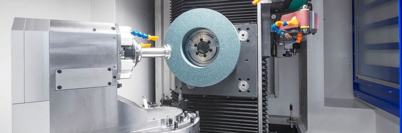 La zone de travail d’une CT 501 avec à gauche l'axe C porte-pièce, la meule est montée dans la broche principale et en haut à droite les deux bandes abrasives.