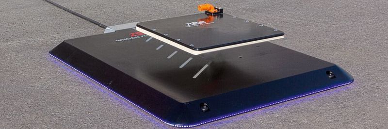 Das Ground Pad eines induktiven Ladesystems mit Bodenspule und das Card Pad mit dem orangen Hochvoltanschluss zur Batterie, das im Fahrzeug verbaut wird.