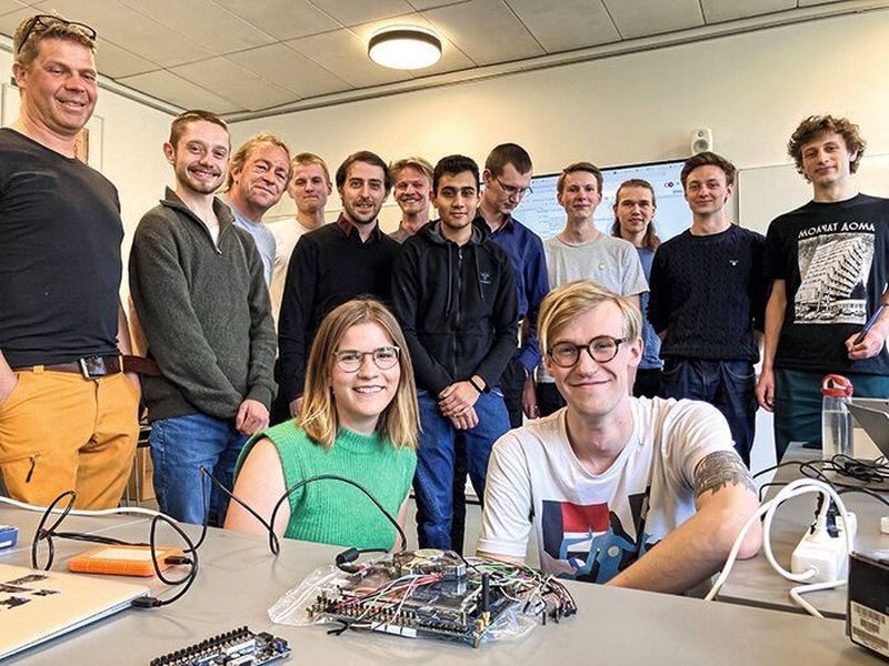 Die 12 Studenten des Chipdesign-Kurses der DTU Electrical Engineering, zusammen mit ihrem Professor Martin Schoeberl (3.v.l.), Analogtechniker Jørgen Kragh Jakobsen von IC Works (links) und der von Ihnen entworfenen Prototypen-Platine. Unter Zuhilfenahme von Open-Source-Tools für Chipdesign, der RISC-V-IP und dem von Google und der Foundry Skywater herausgegebenen quelloffenen Process Design Kits konnte der von den Studenten entworfene Dual-Core-Chip komplett mit Open-Source-Mitteln entworfen, entwickelt und gefertigt werden.