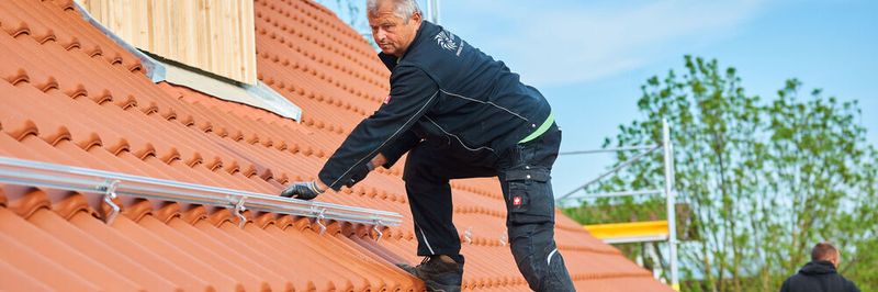 Ein Monteur montiert eine Solarmodul-Unterkonstruktion auf einem Dach