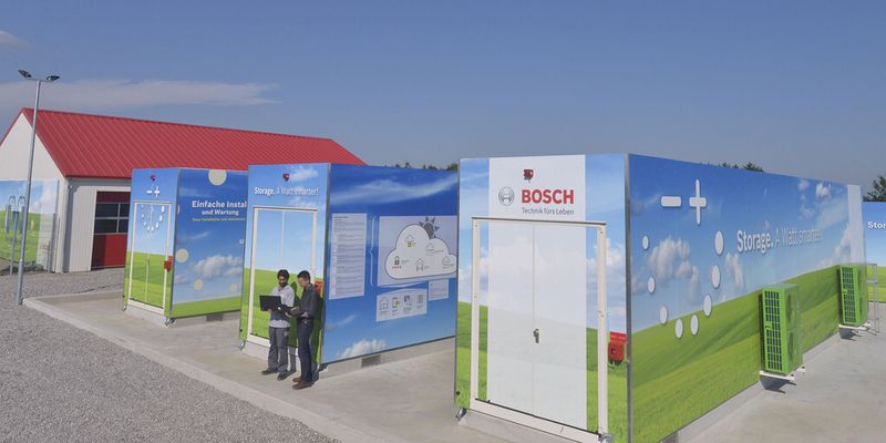 Im Vordergrund sind die drei großen Container zu sehen, in denen die Lithium-Ionen-Akkus untergebracht sind. Das Gebäude im Hintergrund beherbergt die Vanadium-Redoxflow-Batterie.