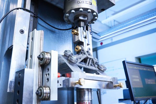 Hier wird am Fraunhofer IWM ein additiv gefertigtes Metallteil in einer Testvorrichtung zyklisch belastet, nachdem seine hochbeanspruchten Oberflächenzonen mechanisch nachbehandelt wurden. Jetzt weiß man schon vor der Fertigung, wo man nachbehandeln muss ...(Bild:  Fraunhofer IWM)