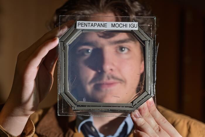Abram Fluckiger holds up a sample panel square that has five sandwiched layers of a new material nearly transparent insulation material called Mochi, which was designed buy CU Boulder researchers in physics professor Ivan Smalyukh’s lab.  (Source: Glenn J. Asakawa/CU Boulder)