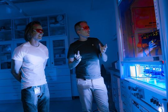 Hinter einer Glasscheibe leuchten LED-Lampen auf kleine Reaktionsgefäße und aktivieren so chemische Reaktionen. Im Bild: ISTA-Wissenschaftler Aleksander Bena (l.) und Bartholomäus Pieber.(Bild:  ISTA)