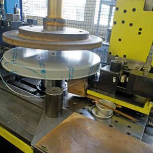 So entstehen die Waagschalen: Ein Werkstück ist zentral geklemmt und rotiert in der Maschine. Die ausgefransten Ränder des tiefgezogenen Blechteils werden geschnitten und gebördelt.
