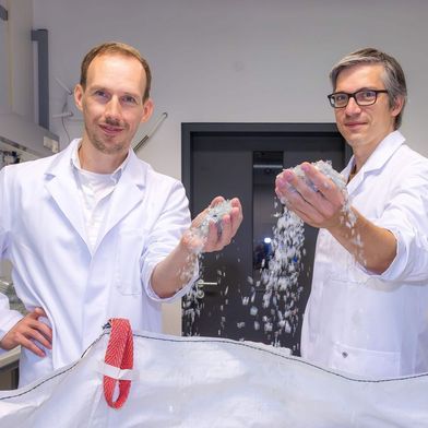 Dr. Ronny Frank (links) und Dr. Christian Sonnendecker vor einem Sack voll kleingehäckselten PET-Obstschalen, die darauf warten, mithilfe des Enzyms PHL7 in ihre chemischen Bausteine zerlegt zu werden. (Bild: Swen Reichhold/Universität Leipzig )