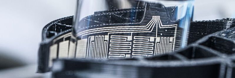 Hält gefühlvoll den Messbecher, statt ihn zu zerbrechen: Durch das Glas sind die integrierten Sensoren der BioGrip-Greifer zu sehen.(Bild:  Fraunhofer IWS)