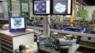 Visuelles Assistenzsystem für einen Arbeitsplatz zur Bestückung von Wechselpaletten. Im Vordergrund ist die drehbar gelagerte Bauteilaufnahme, im Hintergrund die Visualisierung auf Bildschirmen mit Kameraüberlagerung und CAD-Darstellung zu sehen.  (Bild: Kolbus)