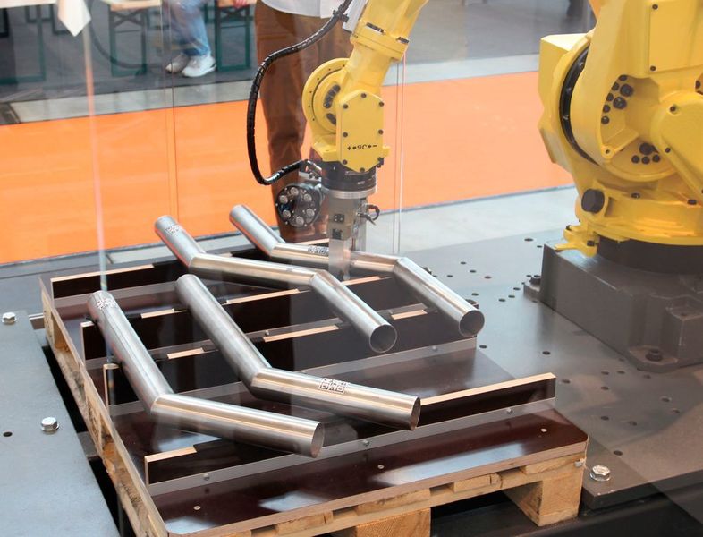 ...derselbe Roboter nimmt sich das Halbzeug und bewegt es in Richtung Bearbeitungsroboter nach oben...Schunk-Technik hat das Rohr dabei sicher im Griff. (Königsreuther)