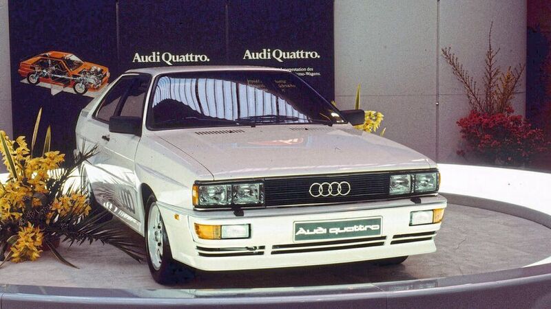 Auf dem Automobilsalon in Genf enthüllt Audi 1980 den Audi quattro (B2), ab Mitte der 1990er-Jahre als Urquattro bezeichnet. Er setzt auf das Triebwerk vom Audi 200 5T (C2), jedoch mit Ladeluftkühlung. Dadurch erreicht das Turbo-Aggregat eine höhere Leistung von 147 kW (200 PS) bei 5.500 Umdrehungen pro Minute und 285 Newtonmeter Drehmoment bei 3.500 Touren. Die Karosserie des Audi quattro basiert auf dem Audi Coupé (B2), das wiederum vom Audi 80 abgeleitet ist. Verbreiterte Kotflügel, voluminösere Stoßfänger und Schweller sowie ein größerer Heckspoiler unterscheiden den Audi quattro vom Coupé. (Audi)