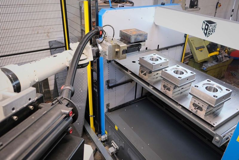 The 70 kg payload capacity robot picking up a fresh billet fixtured it in a vice from the top drawer of the Tezmaksan cell for transportation to the VMC. Finish-machined oil and gas industry components are awaiting removal from the other three vices. (Source: Whitehouse Machine Tools )