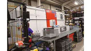 Während eine Mitarbeiterin rechts die zu reinigenden Bauteile in durchlässigen Gitterkörben auf das Zuführsystem setzt, nimmt eine Kollegin auf der linken Seite die gereinigten Bauteile wieder vom Band. Dazwischen findet in der Pero R2 automatisch die Reinigung mit Lösemittel in Vollvakuum statt. (Bild: Pero)