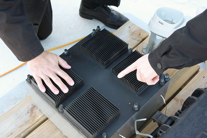 Die Nahaufnahme zeigt den thermischen Resonator (Black Box) mit seinen Kühlrippen über der Oberseite. Das Gerät ist mit einem Phase-Change-Material gefüllt, das es ermöglicht, Energie aus wechselnden Temperaturen aufzunehmen. (Melanie Gonick / MIT)