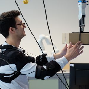 Forscher Federico Masiero nimmt ein Päckchen von einem Roboter (von Neura Robotics) entgegen.(Bild:  Andreas Schmitz / TUM)