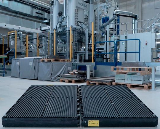 Die beiden schwarzen Bauteile vor dieser Wickert-Presse haben bewiesen, dass man leichte Batteriegehäuse für die E-Mobilität wirtschaftlich auch aus faserverstärkten Thermoplasten herstellen kann. Das brachte dem Team der TU Chemnitz den JEC Innovation Award 2026 ein.(Bild:  TU Chemnitz)
