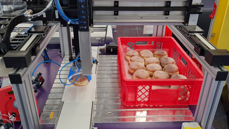 Der Roboter nimmt die fertigen Berliner vom Förderband und legt sie schonend in die Transportbox. (Bild:  Igus GmbH)