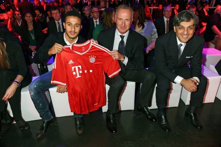 (v. li.): Thiago Alcantara, Karl-Heinz Rummenigge (beide FC Bayern München) und Luca de Meo (Vertriebsvorstand Audi) freuen sich über das Trikot des FC Bayern, das zukünftig die Ausstellungshalle schmücken wird. (Foto: Audi)