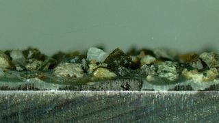 Die Mikroskopaufnahme zeigt den Schnitt durch ein Stahlbauteil auf dessen Oberfläche mit einem organischen Klebstoff ein Granulat angebunden wurde. Zwei so vorbereitete Bauteile werden dann mit einem anorganischen Klebstoff fest verbunden. (KIT)