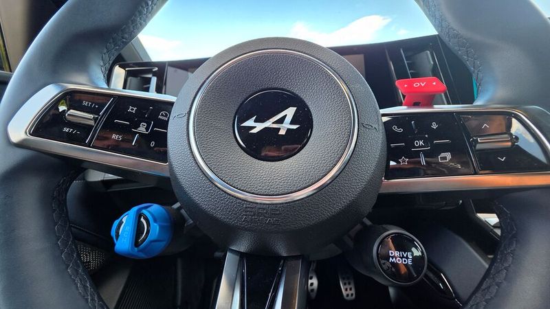 4. Die Tasten am Lenkrad: Auch am Lenkrad-Layout erkennt man die Sportwagenseele der Alpine A390. Der blaue RCH-Drehschalter regelt den vierstufigen Rekuperationsgrad bis zum One-Pedal-Modus, die rote OV-Taste steuert hingegen den Boost für Überholvorgänge. Drückt man sie, rufen die Motoren die volle Leistung ab, und das Sport-Fastback wird für maximal zehn Sekunden förmlich nach vorne katapultiert. Auch die Fahrmodi lassen sich über eine Taste am Lenkrad auswählen. Insgesamt hat der Fahrer die Wahl zwischen fünf Fahrmodi. Neben dem Sport-Modus gibt es auch einen Track-Modus. Ausprobiert haben wir diesen Modus nicht, da er speziell für die Rennstrecke gedacht ist. So wird unter anderem das ESP extrem gelockert und die Balance  stärker auf die Hinterachse verlagert. Gleichzeitig sprechen die Motoren und die Lenkung extrem schnell an.  (Bild: Mauritz – VCG)